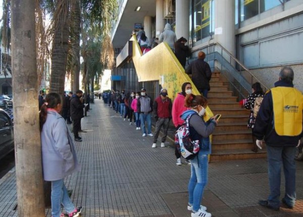 Beneficiarios de planes sociales haciendo cola con barbijos